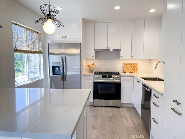 kitchen featuring light wood finished floors, decorative backsplash, appliances with stainless steel finishes, white cabinetry, and a sink