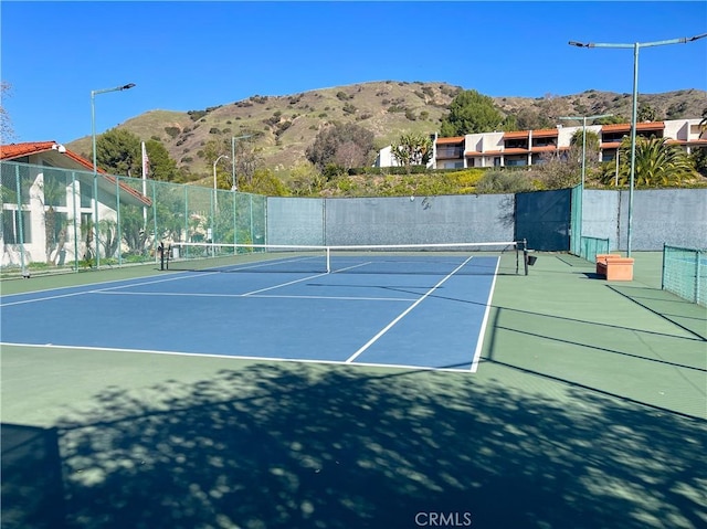 view of tennis court with a mountain view and fence