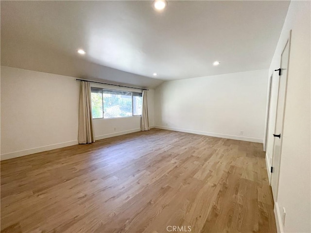 empty room featuring light wood-type flooring, vaulted ceiling, baseboards, and recessed lighting