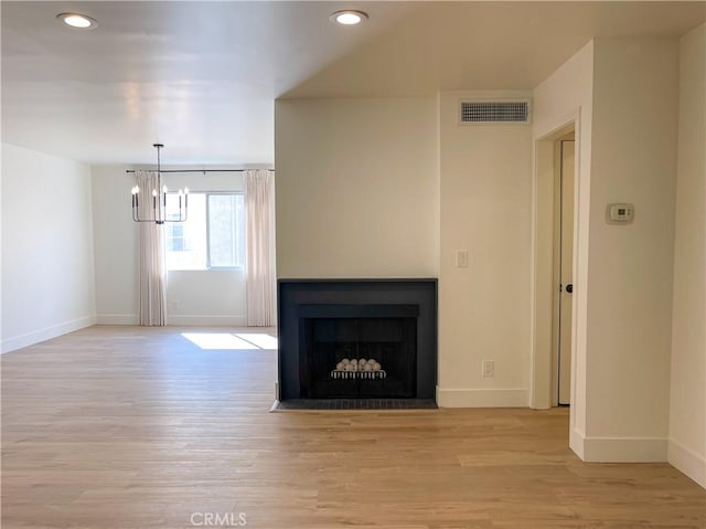 unfurnished living room featuring light wood-style floors, a fireplace with flush hearth, visible vents, and baseboards