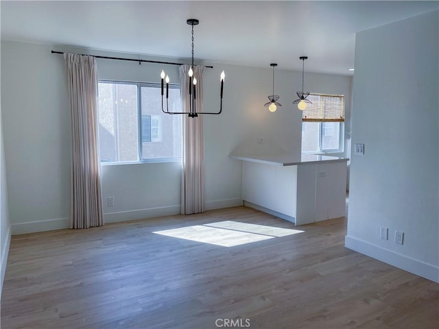 unfurnished dining area featuring a notable chandelier, wood finished floors, and baseboards