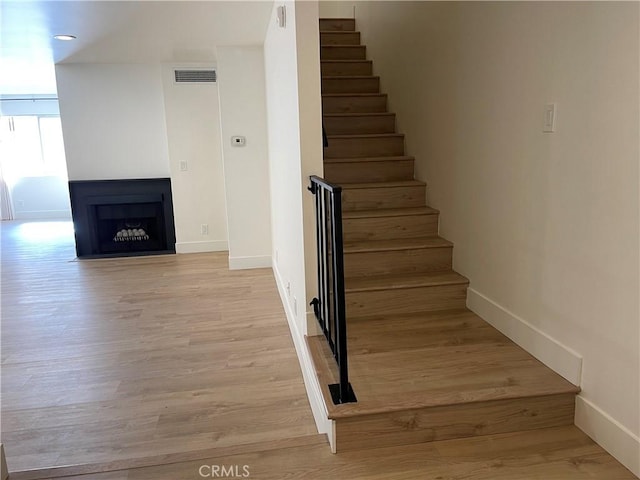 staircase with a fireplace, wood finished floors, visible vents, and baseboards