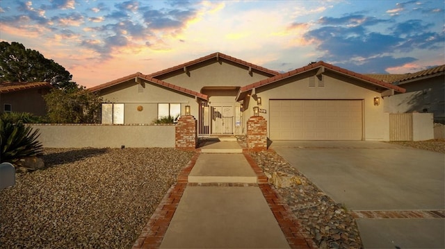 mediterranean / spanish-style home featuring brick siding, a tiled roof, concrete driveway, stucco siding, and an attached garage