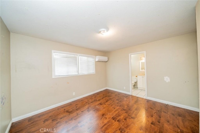 empty room with baseboards, an AC wall unit, and wood finished floors