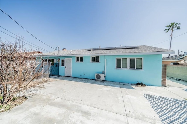 rear view of property featuring ac unit, a patio, stucco siding, roof mounted solar panels, and fence