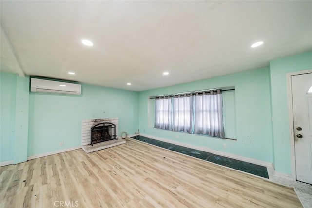 unfurnished living room with baseboards, a fireplace with raised hearth, wood finished floors, a wall mounted AC, and recessed lighting