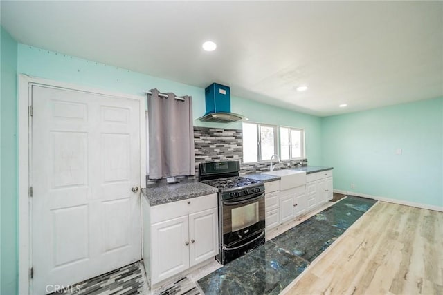 kitchen featuring backsplash, white cabinetry, black gas stove, wall chimney range hood, and a sink