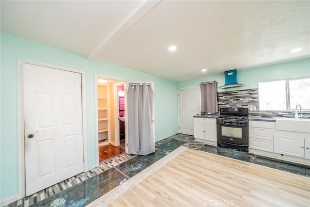 kitchen featuring black gas range, a sink, exhaust hood, white cabinets, and tasteful backsplash