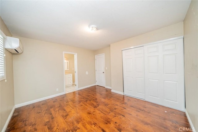 unfurnished bedroom featuring a closet, baseboards, wood finished floors, and a wall mounted AC