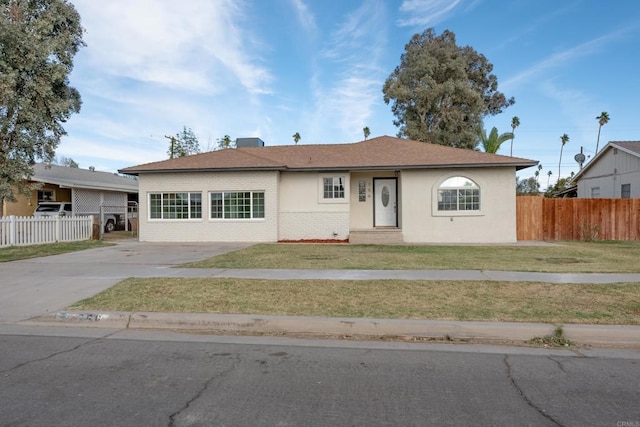 single story home with concrete driveway, brick siding, fence, and a front lawn