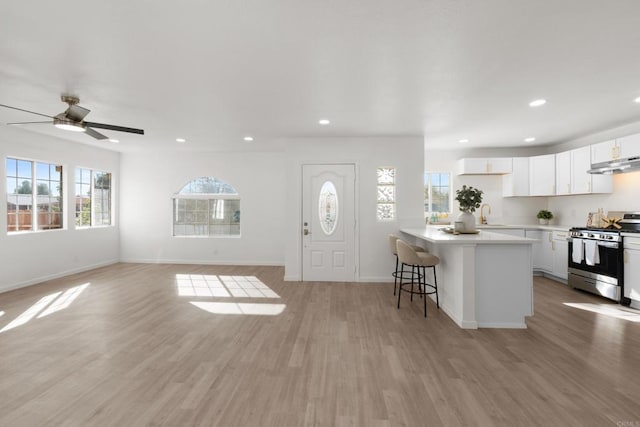 kitchen featuring stainless steel gas range, light countertops, light wood-type flooring, a kitchen bar, and white cabinetry