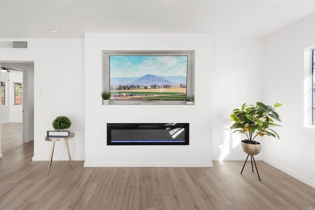 unfurnished living room featuring a glass covered fireplace, visible vents, baseboards, and wood finished floors