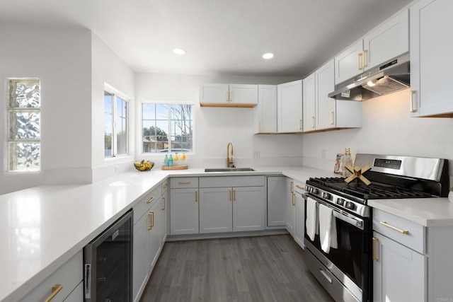 kitchen with light wood-style flooring, wine cooler, under cabinet range hood, stainless steel range with gas cooktop, and a sink