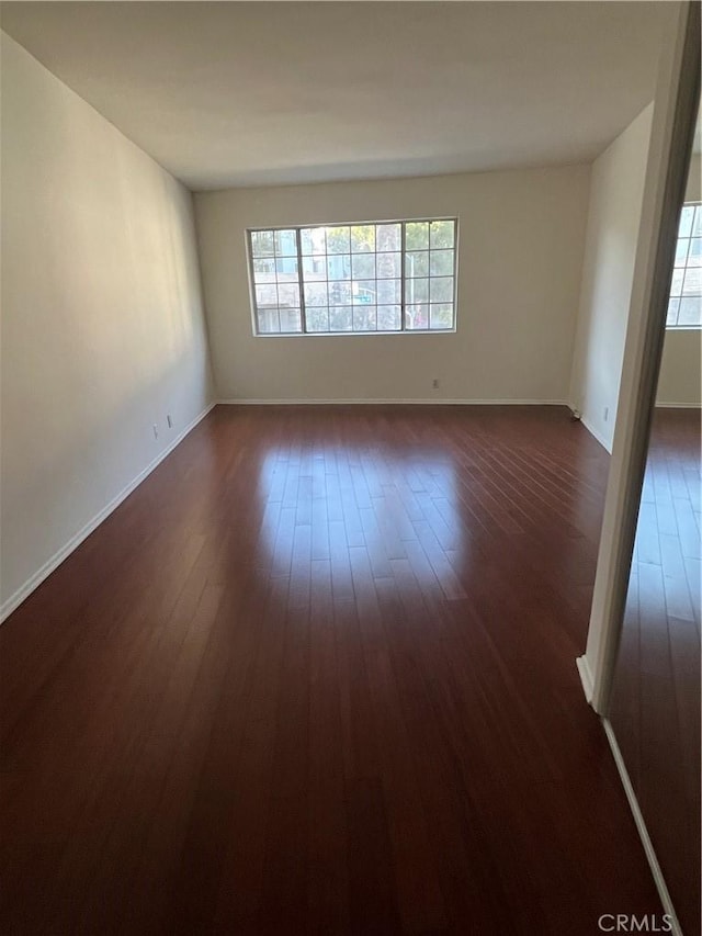 unfurnished room with dark wood-type flooring, a healthy amount of sunlight, and baseboards