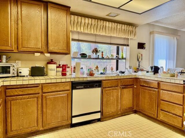 kitchen with brown cabinetry, dishwasher, and light floors