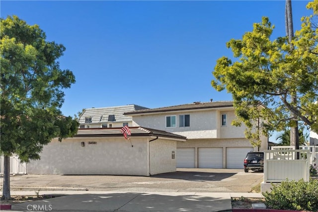 view of front of house featuring a garage, concrete driveway, fence, and stucco siding