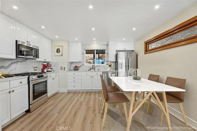 kitchen with light countertops, light wood finished floors, tasteful backsplash, appliances with stainless steel finishes, and white cabinets