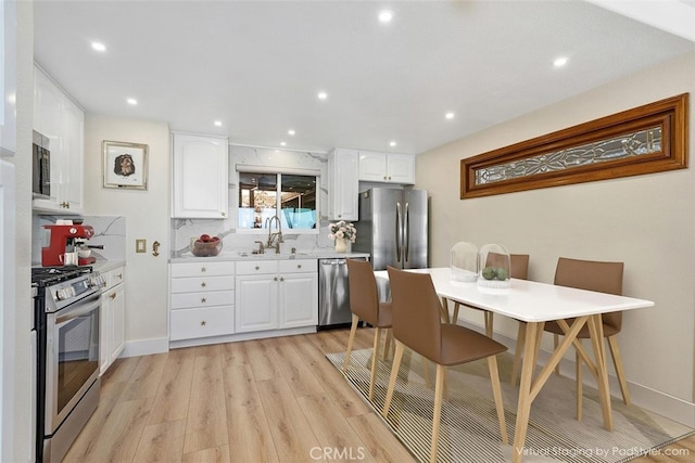 kitchen featuring white cabinets, a sink, stainless steel appliances, and light wood-style floors