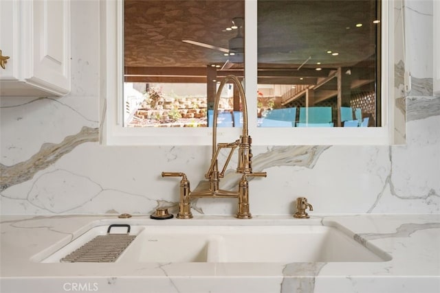 interior details featuring backsplash, white cabinets, light stone countertops, and a sink