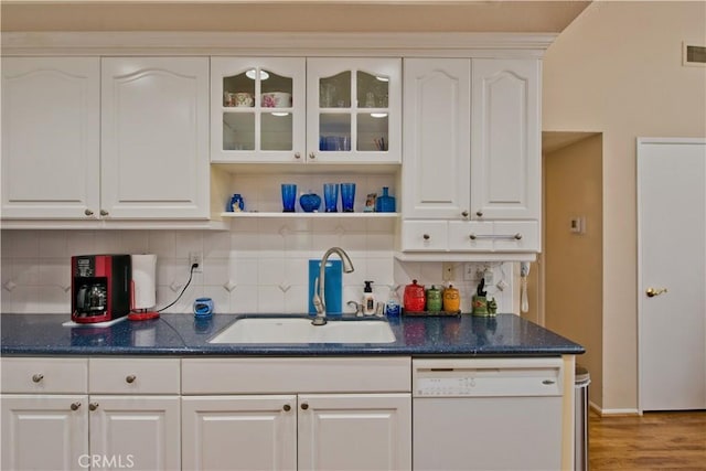 kitchen with white dishwasher, decorative backsplash, white cabinets, and a sink