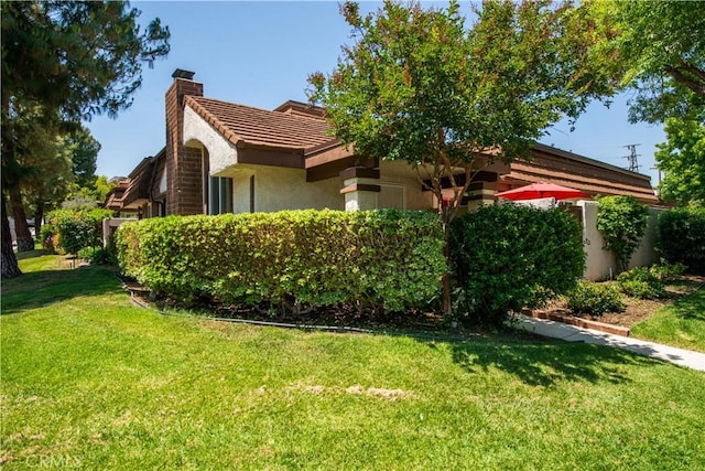 view of home's exterior with a tile roof, a yard, a chimney, and stucco siding