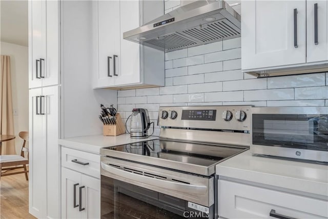 kitchen featuring electric stove, decorative backsplash, wall chimney range hood, light countertops, and white cabinets