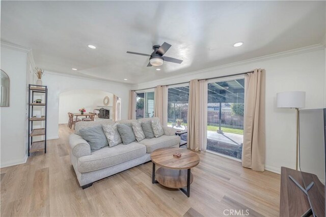 living area with baseboards, arched walkways, ceiling fan, ornamental molding, and light wood-type flooring