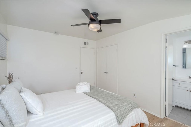 bedroom with a closet, ensuite bathroom, light wood finished floors, baseboards, and visible vents