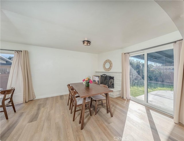 dining area with baseboards, light wood-style floors, and a fireplace with raised hearth