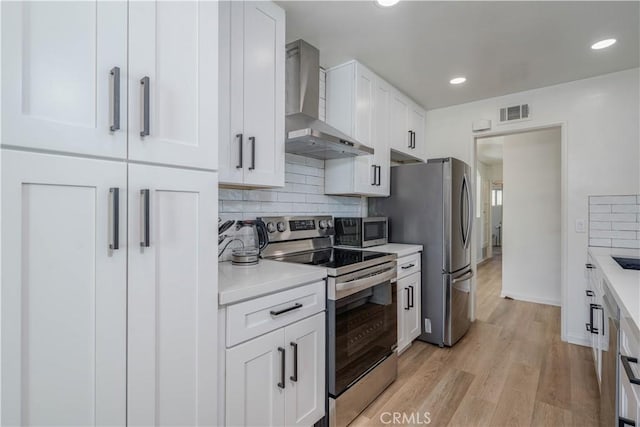 kitchen with white cabinets, wall chimney exhaust hood, appliances with stainless steel finishes, and light countertops