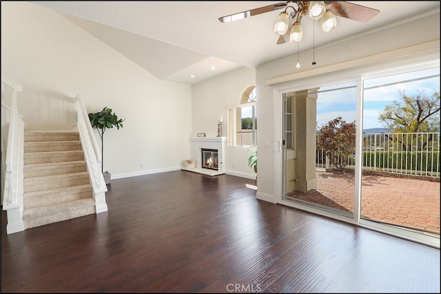 unfurnished living room featuring a brick fireplace, baseboards, dark wood finished floors, stairway, and a ceiling fan