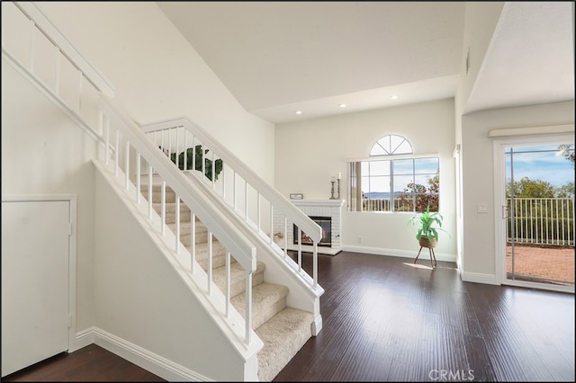 stairway with baseboards, a high ceiling, wood finished floors, and a fireplace