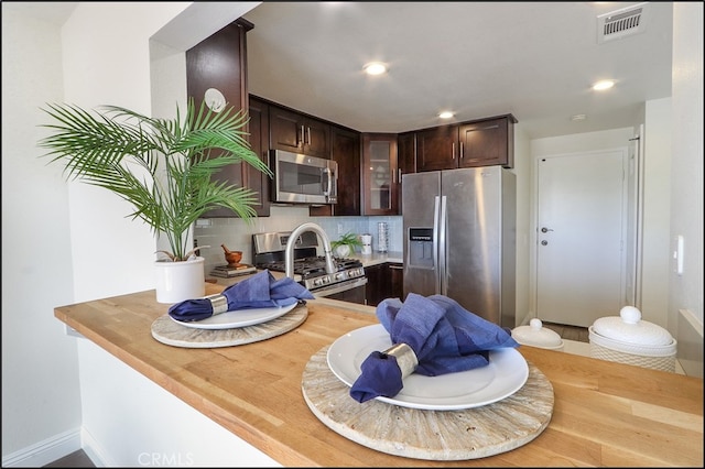 kitchen featuring visible vents, tasteful backsplash, dark brown cabinetry, appliances with stainless steel finishes, and glass insert cabinets