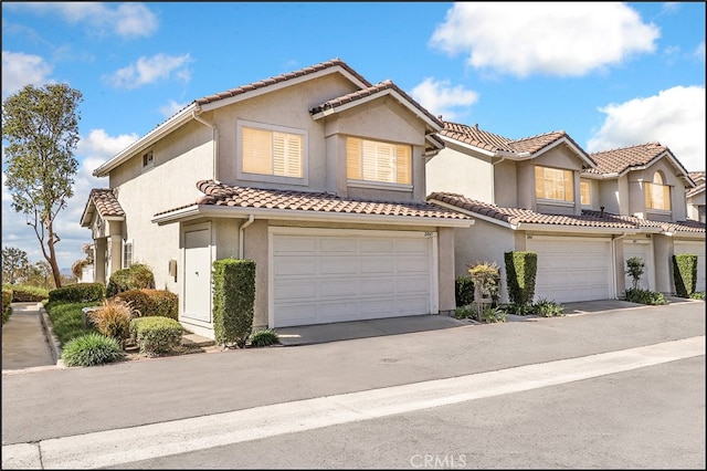 view of front of home with a tile roof, an attached garage, driveway, and stucco siding