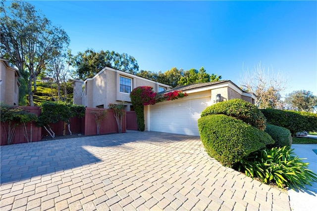 exterior space with a garage, decorative driveway, fence, and stucco siding