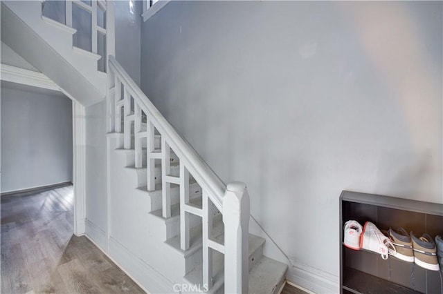 stairway featuring baseboards, a high ceiling, and wood finished floors