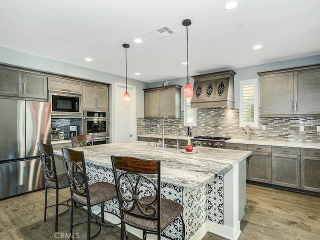 kitchen featuring wood finished floors, visible vents, appliances with stainless steel finishes, custom exhaust hood, and decorative backsplash