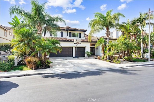 mediterranean / spanish home featuring concrete driveway, a tile roof, an attached garage, and stucco siding