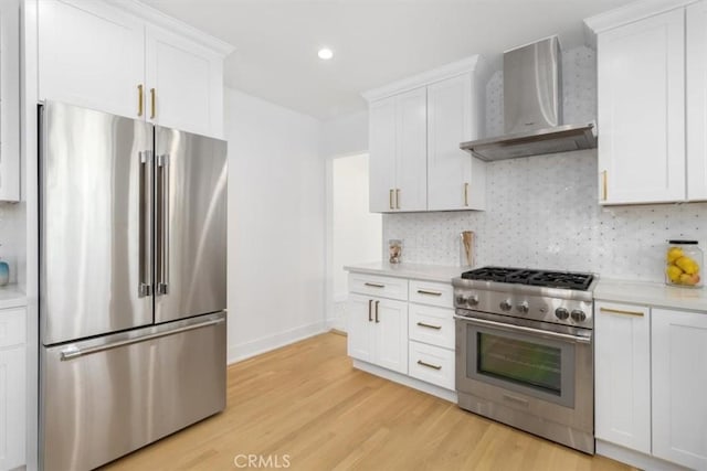 kitchen featuring high end appliances, tasteful backsplash, light countertops, wall chimney range hood, and light wood-type flooring