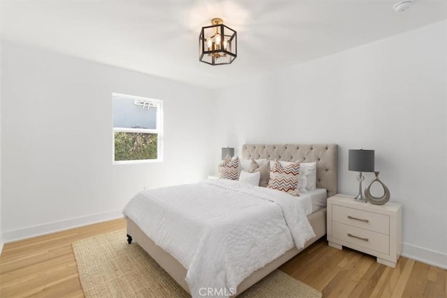 bedroom featuring a notable chandelier, light wood-type flooring, and baseboards