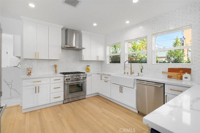 kitchen with light wood finished floors, stainless steel appliances, visible vents, a sink, and wall chimney exhaust hood