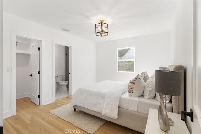 bedroom featuring a chandelier, light wood-type flooring, a walk in closet, and visible vents