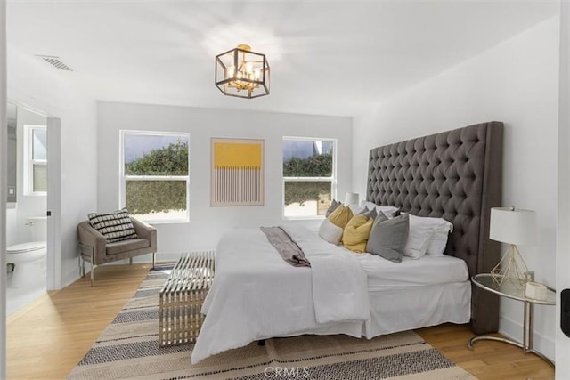 bedroom with a chandelier, visible vents, connected bathroom, and wood finished floors