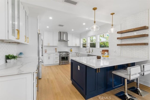 kitchen featuring a peninsula, wall chimney range hood, appliances with stainless steel finishes, and white cabinetry