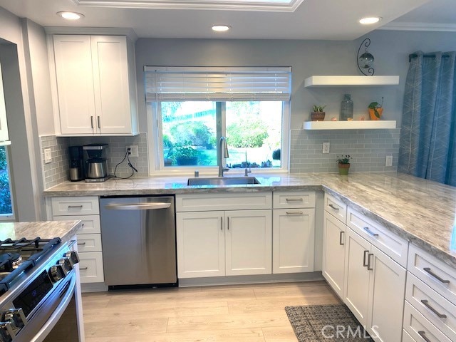 kitchen featuring light wood finished floors, appliances with stainless steel finishes, white cabinets, a sink, and light stone countertops