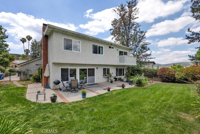 rear view of house featuring a lawn, stucco siding, and a balcony