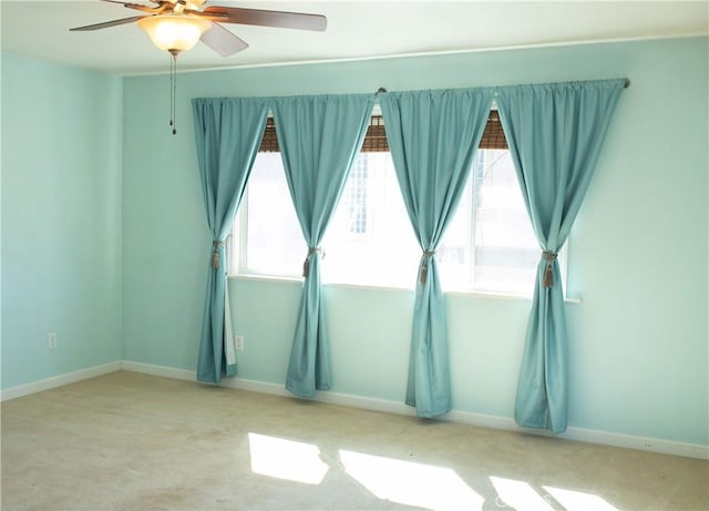 carpeted spare room featuring ceiling fan and baseboards