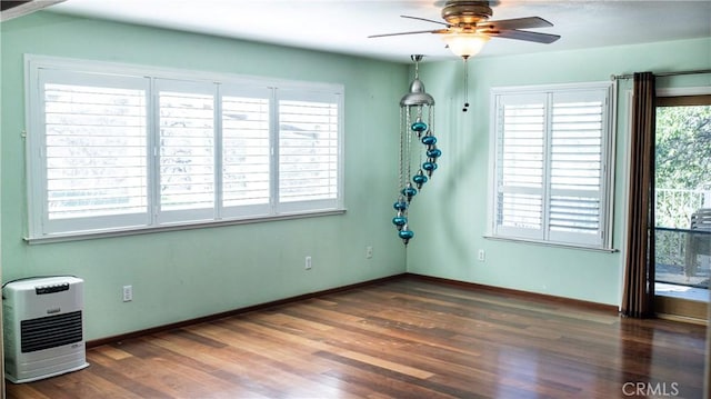 empty room with baseboards, ceiling fan, heating unit, and wood finished floors