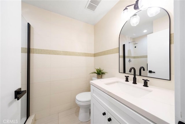 bathroom with toilet, a shower with shower door, vanity, visible vents, and tile walls