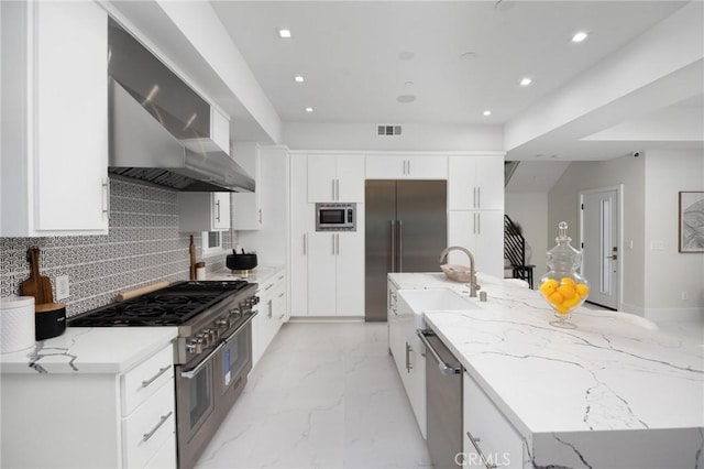 kitchen with marble finish floor, backsplash, white cabinetry, wall chimney range hood, and built in appliances